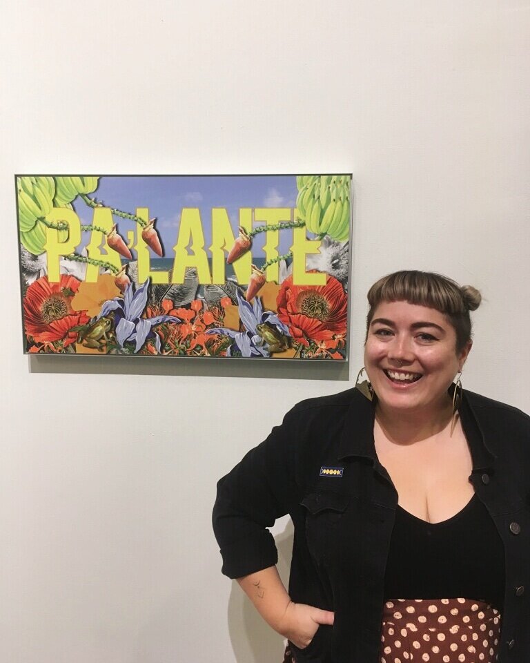 Lares Feliciano wearing a black shirt, blunt bang, hair up and a big smile standing in front of her beautiful artwork