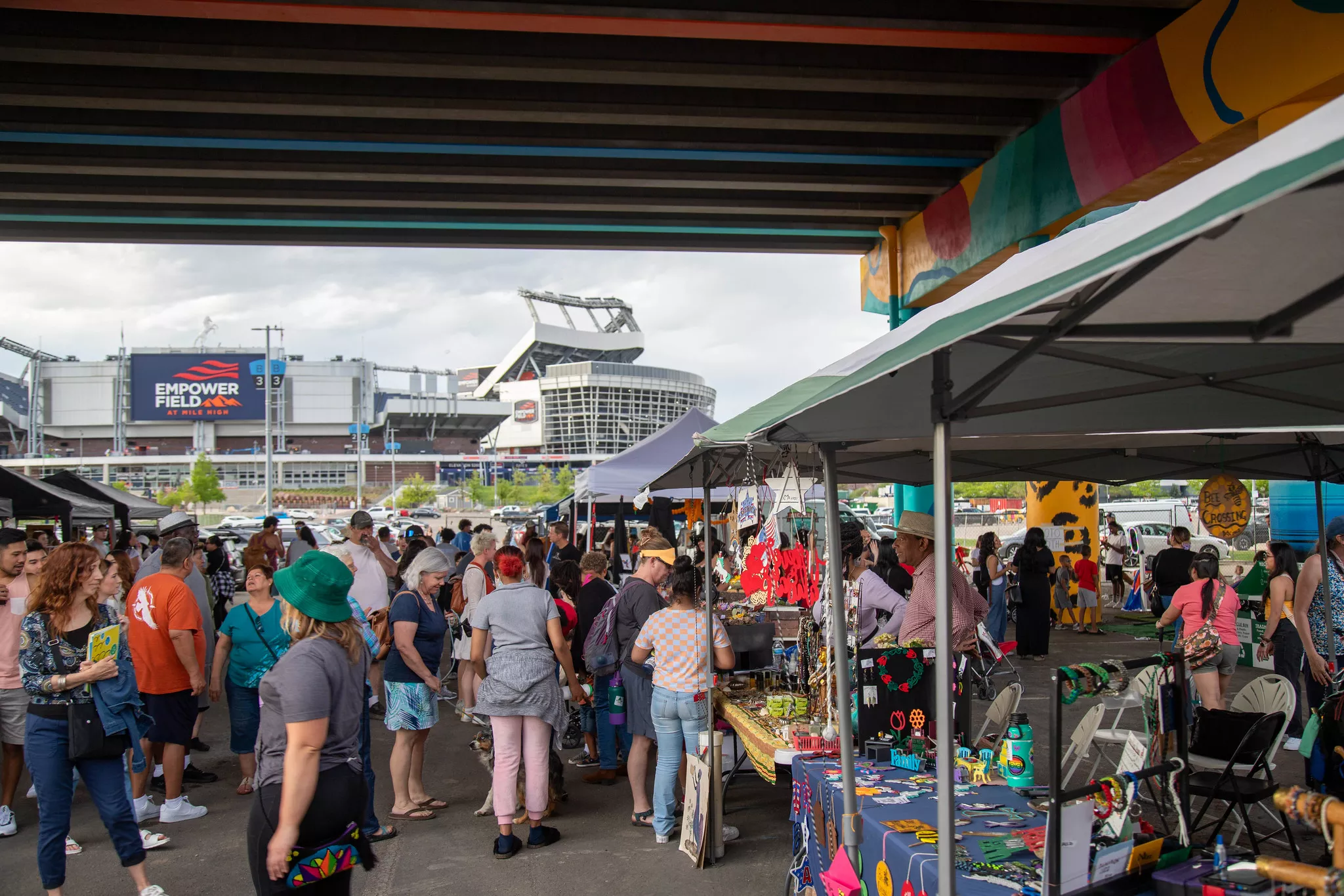 People gather at a night market under the Colfax Street Viaduct in Denver, with Empower Field in the background.