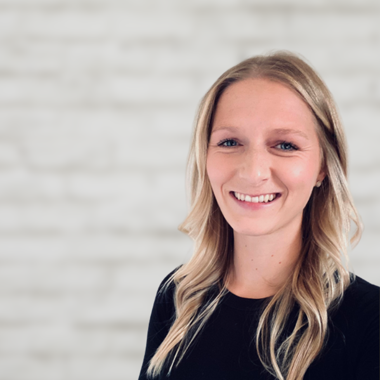 Dana Bakshani is smiling and looking at the camera. She has long blonde hair and blue eyes. She is wearing a black long sleeve shirt. 