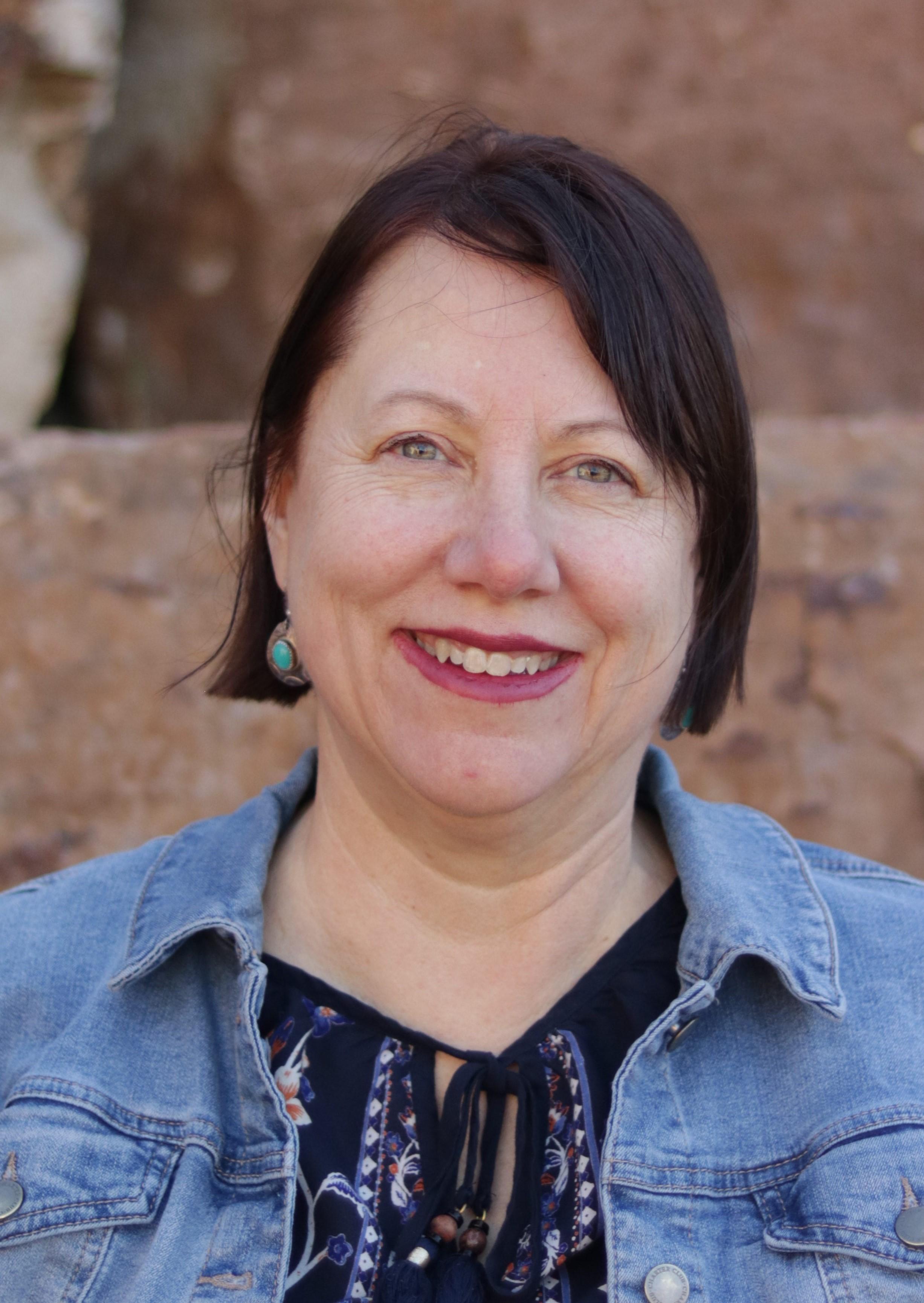 Headshot of Kristin Stephens. She is in front of a rock wall and wearing a jean jacket