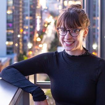 Emma Howard wearing a black turtleneck, standing in front of skyscrapers in early evening 