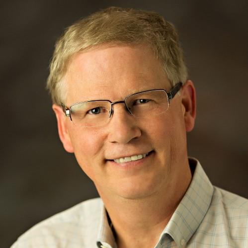 Sam Taylor wearing glasses and a beige collared shirt, pictured smiling