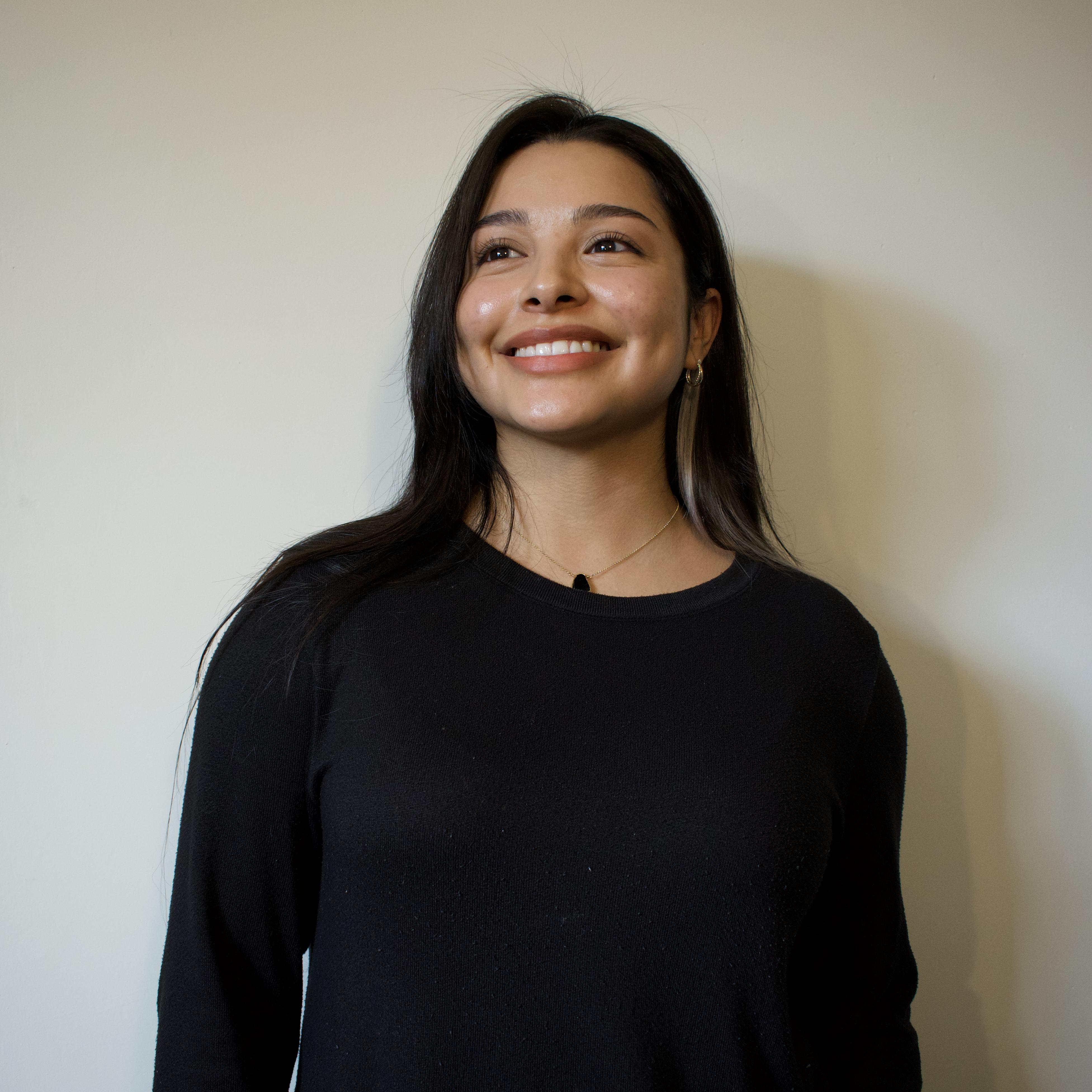 A headshot of Marketing and Operations Coordinator, Frida Silva, with long, straight black hair and a black long sleeves. She's smiling to the side.
