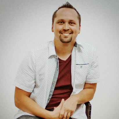 Headshot of Brandon Naughton, who is smiling, sitting on a chair with a white shirt.