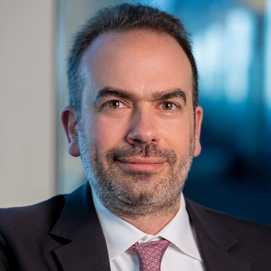 Headshot of George Karayiannakis, smiling, black suit jacket, red tie with designs