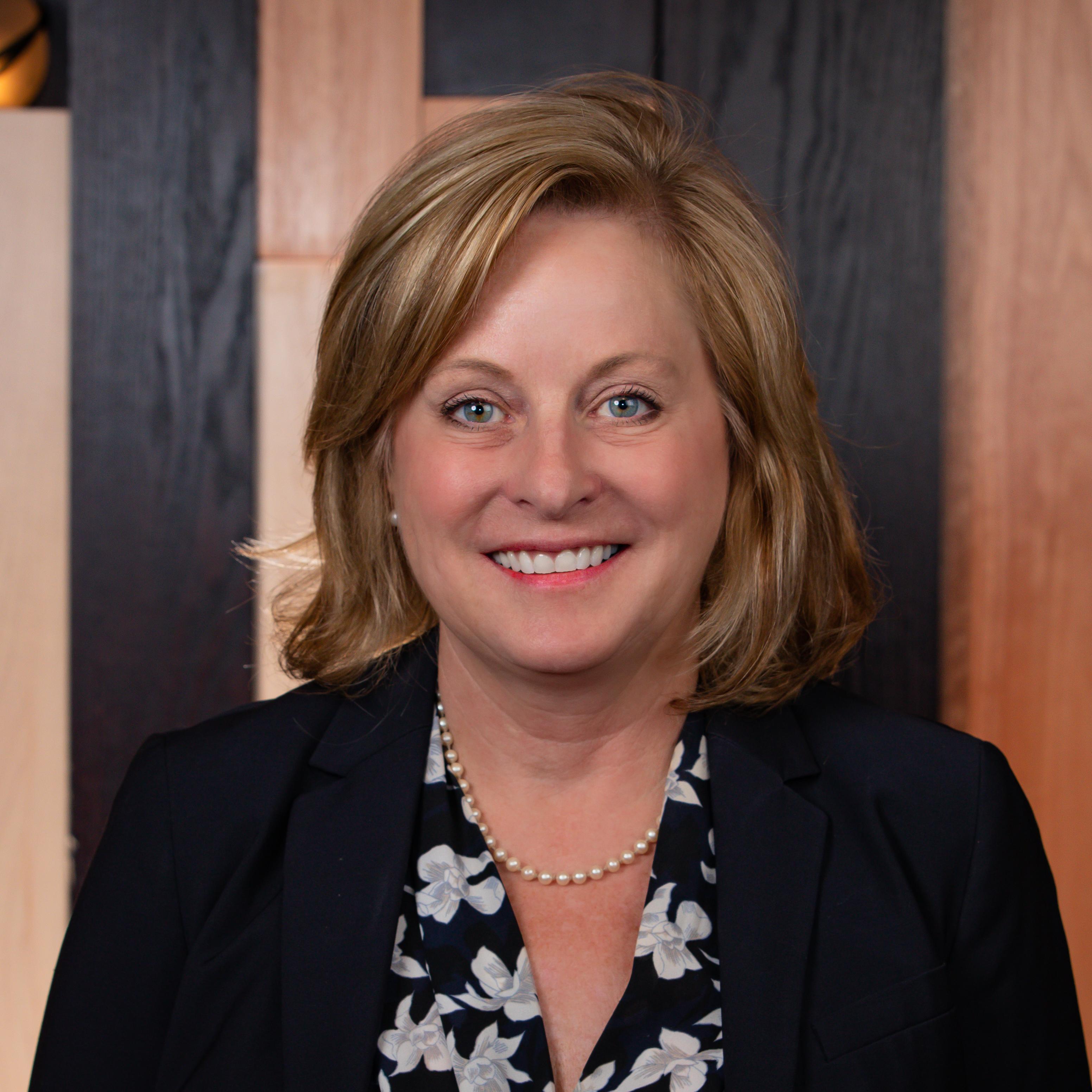 Headshot of Lisa Boyer, smiling, wearing a pearl necklace, wearing a black suit jacket and floral blouse