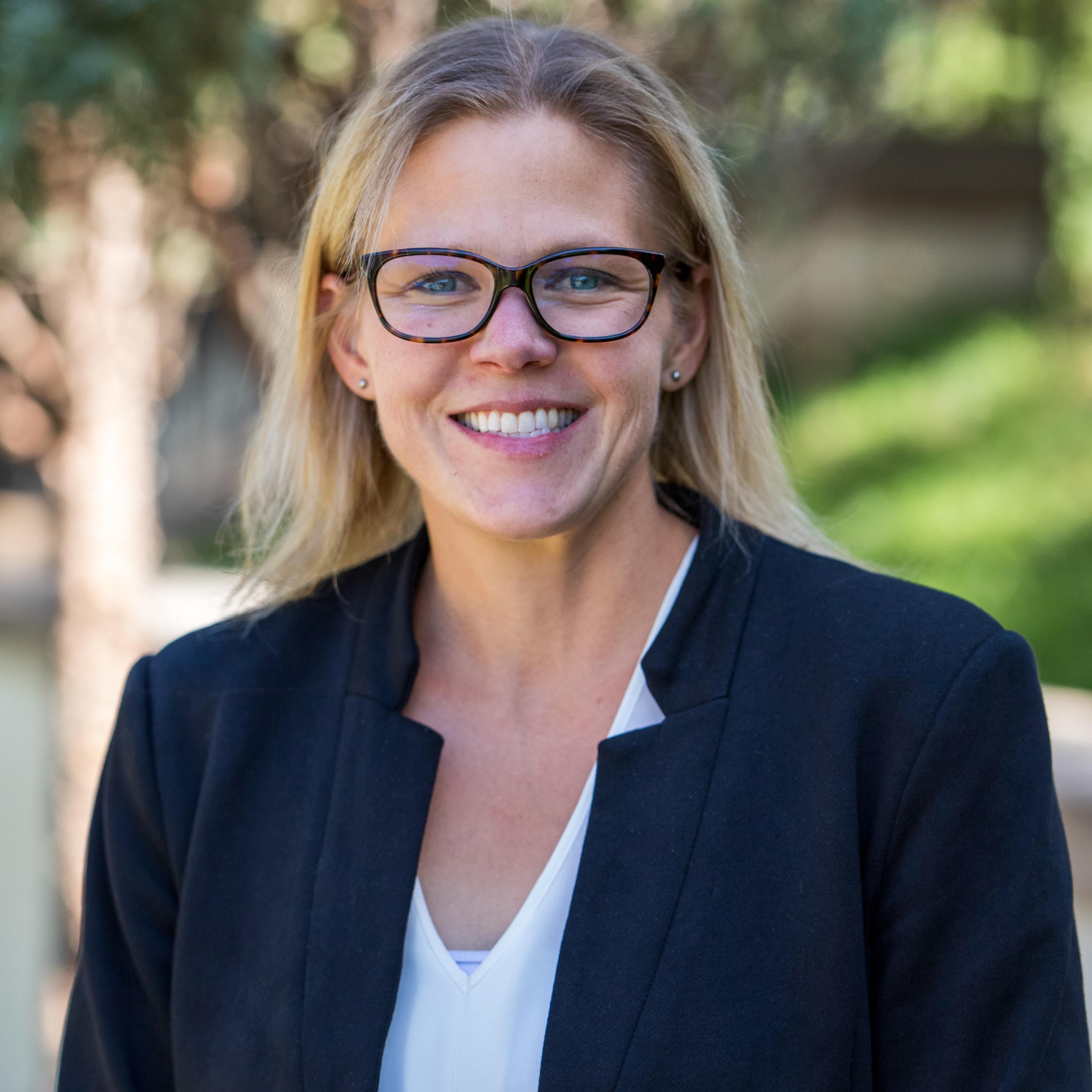 Headshot of Megan Leatham, smiling, black glasses, black suit jacket, white blouse