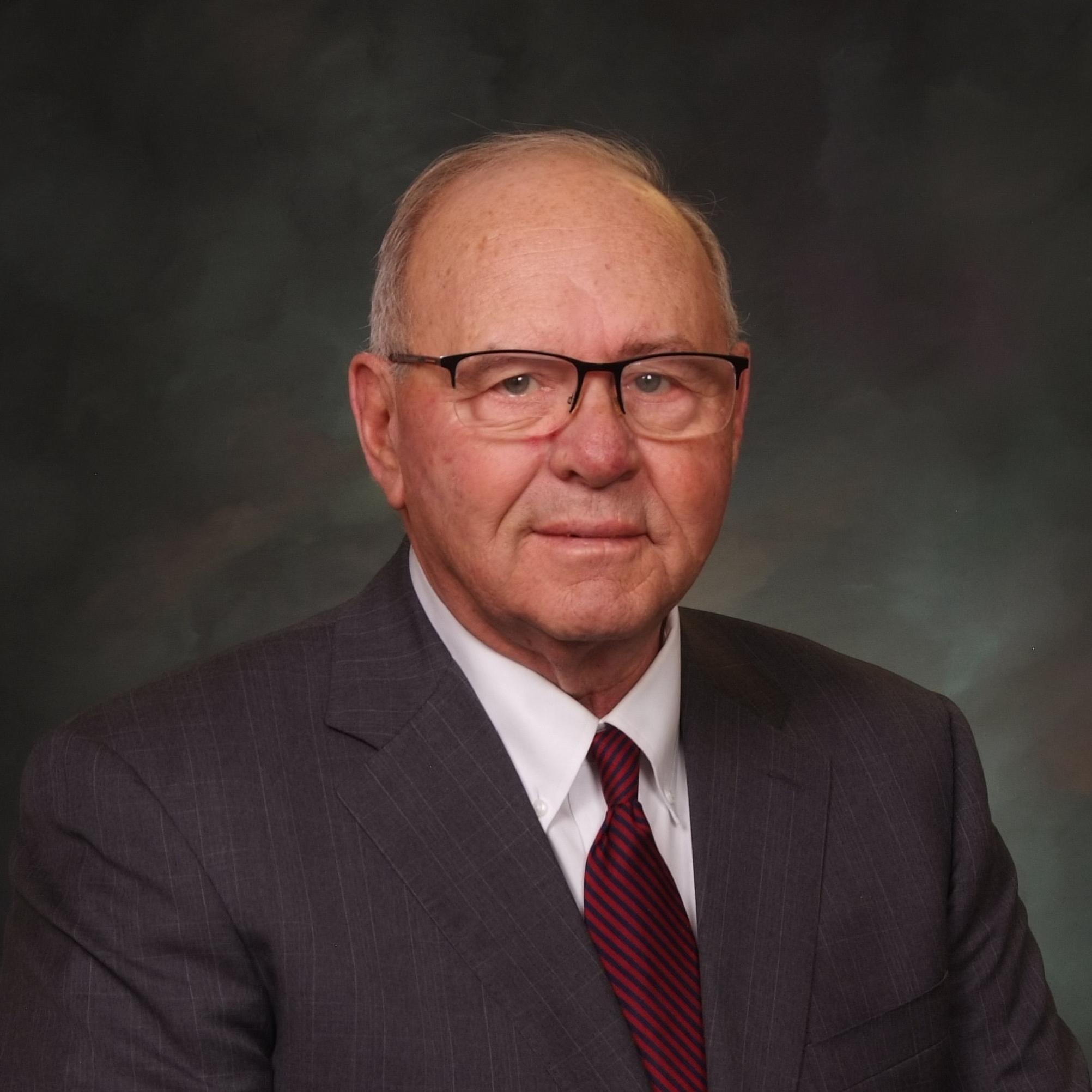 Headshot of Senator Marc Catlin, glasses, dark gray suit jacket, red striped tie.