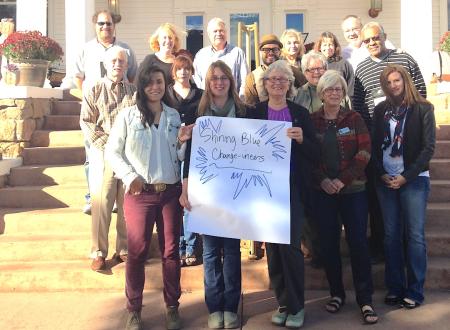 16 change leaders pose on steps in front of a white colonial style building. one woman in the front of the group holds a poster that says shining blue change leaders in blue marker