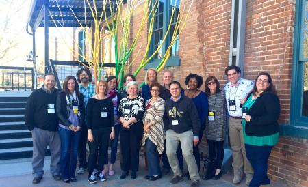 15 change leaders pose in a line in front of a brick industrial building
