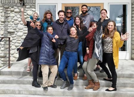 12 change leaders pose in a cluster on concrete stairs in front of a white stone covered building