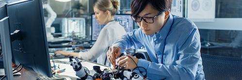 Photo of man wearing glasses building a robotic device