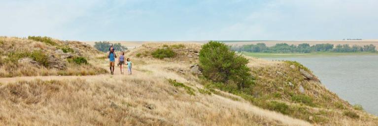 Two adults accompanied by two small children, one on the dads shoulders and one walking alongside mom, on a path which is surrounded by dead grass