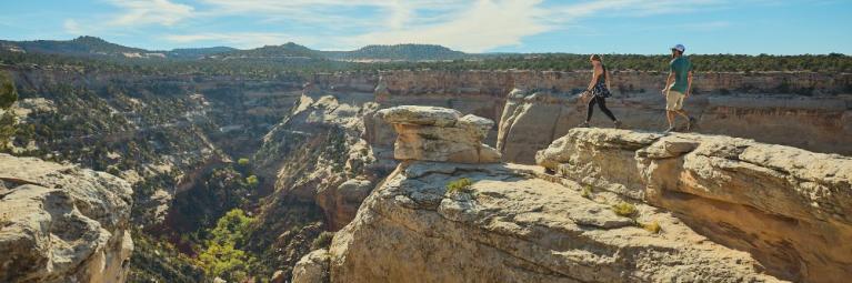 Two hikers approach a cliff's edge looking over a deep valley