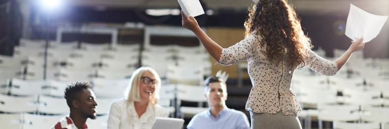 Women holding papers in auditorium with three other people