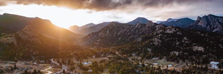 The sun setting over a mountain range, with some deep blue clouds in the background