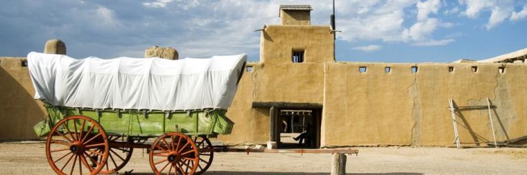 A covered wagon sits in front of a historic fort in La Junta, with blue skies and clouds in the background