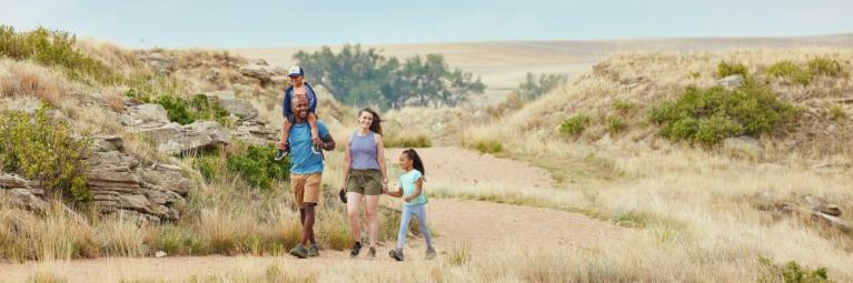 A family of four hikes a dirt path in Yuma County on a sunny day, surrounded by grassy plains 