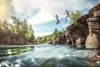 Two people jump off a rocky outcropping in to a river on a sunny day.